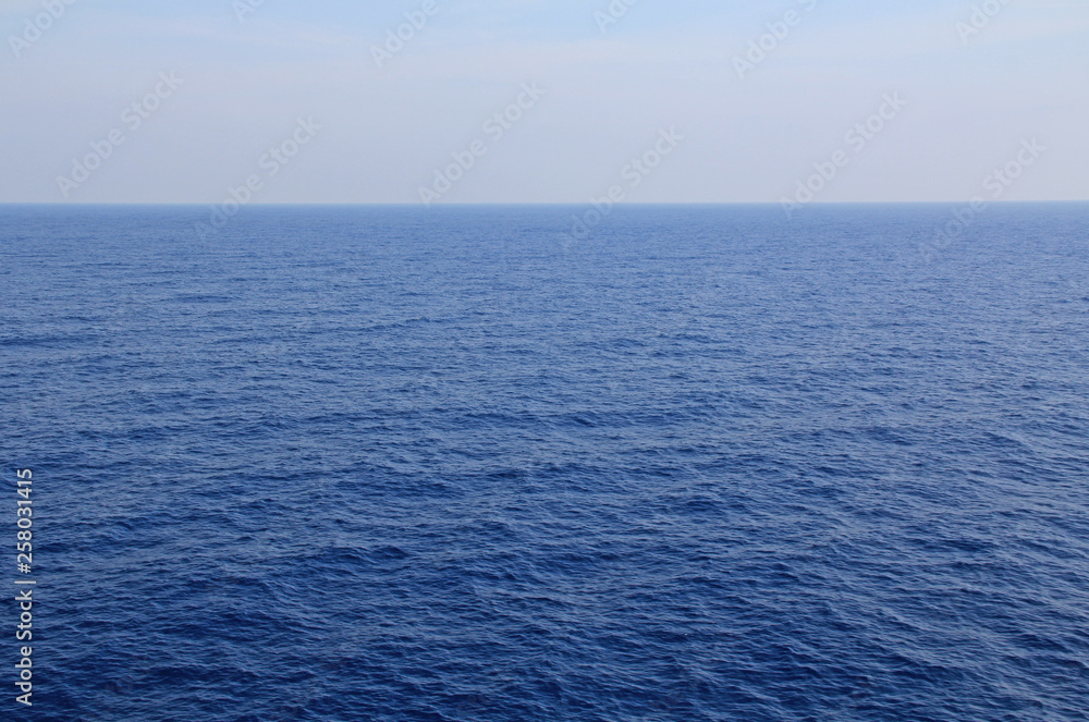 A textured background of the calm open water of the Agean sea with plenty of beautiful blue sky and water copy space.
