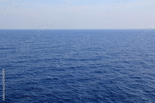 A textured background of the calm open water of the Agean sea with plenty of beautiful blue sky and water copy space.