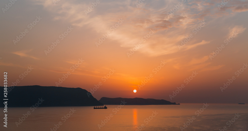 Cargo ship sailing away against orange sunset 