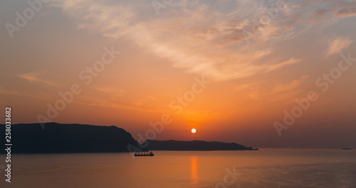 Cargo ship sailing away against orange sunset  © muratart