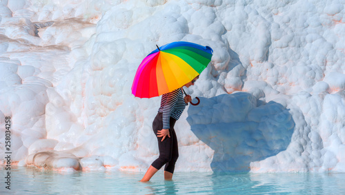 Woman holding multicolored umbrella on the turqouise travertine terraces at Pamukkale (Cotton castle) 
