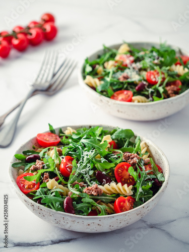 Warm salad with tuna, arugula, tomatoes ,red bean, pasta.Idea and recipe for healthy lunch or dinner.Two bowls with warm salads on marble table. Ideas and recipes for healthy dinner or lunch. Vertical