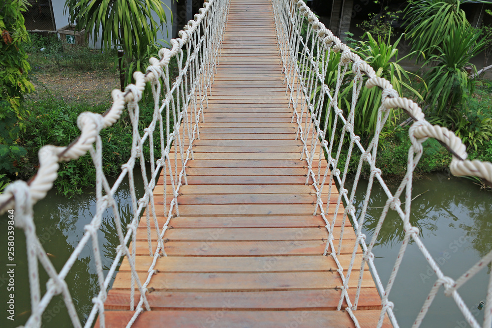 Wooden rope suspension bridge for walk crossing river.
