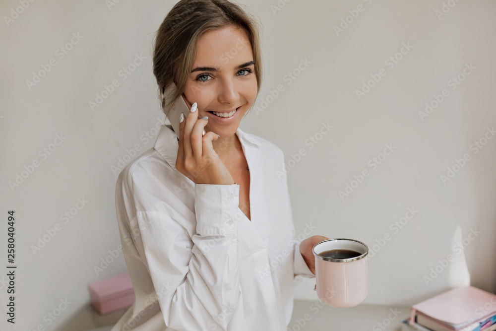 Charming pretty lady with blond hair and fantastic smile talking on the phone while working on modern stylish office Charming pretty lady with blond hair and fantastic smile talking on the phone while working on modern stylish office