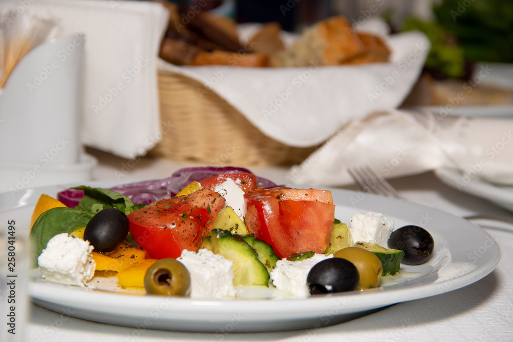 Tasty salad with cheese olives with olives cucumber and tomato on a white plate in the background sliced bread Tasty salad with cheese olives with olives cucumber and tomato on a white plate in the background sliced bread