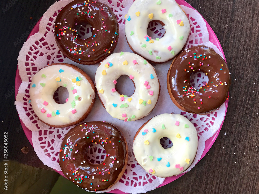 American donuts, glazed with melted chocolate and decorated with sprinkling, lie on a platter.