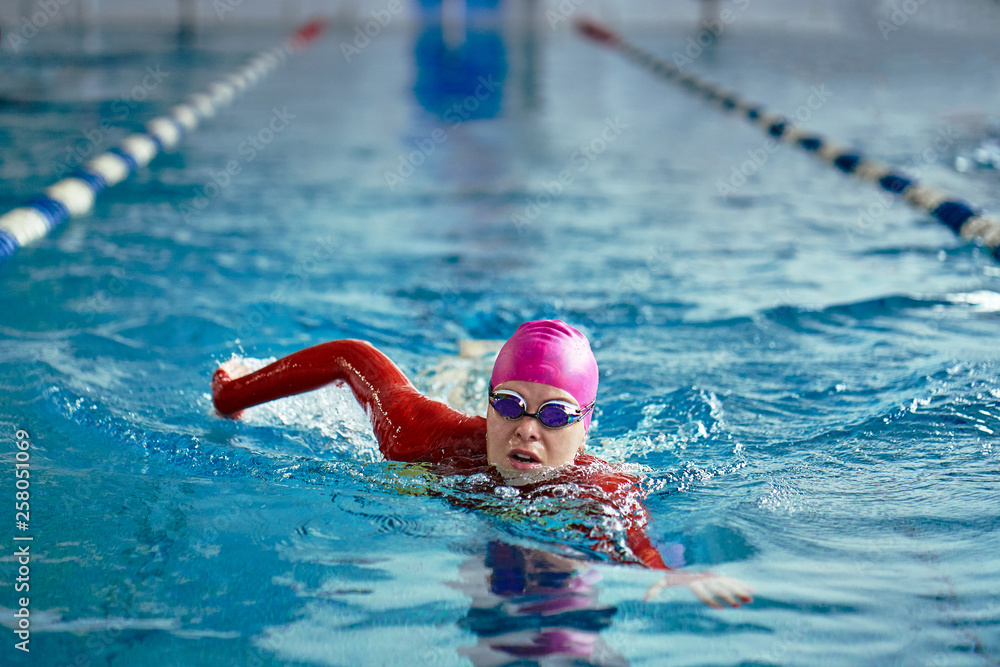 Female athlete swimming fast in crawl style.  Splashes of water scatter in different directions.