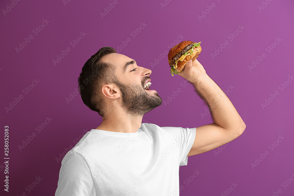 Man eating tasty burger on color background Man eating tasty burger on color background