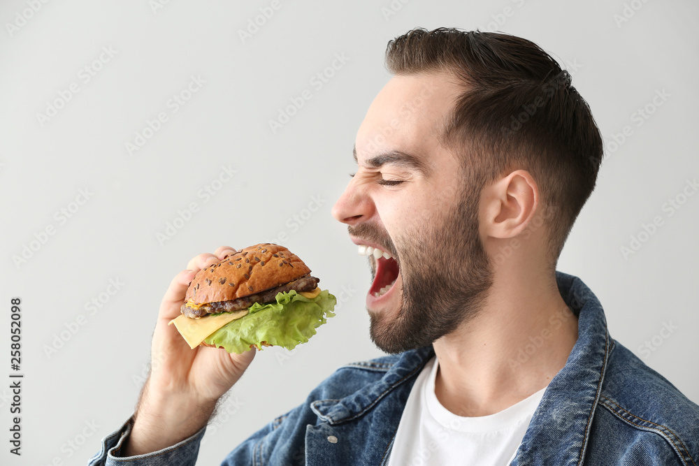 Man eating tasty burger on light background Man eating tasty burger on light background