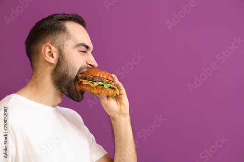 Man eating tasty burger on color background photo