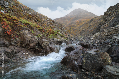 Mountain stream in the gorge. Severe northern landscape with rocks, hills, tundra and low clouds. Arctic nature. Mountain Storm, Chukotka, Siberia, Far East of Russia. Extreme North.