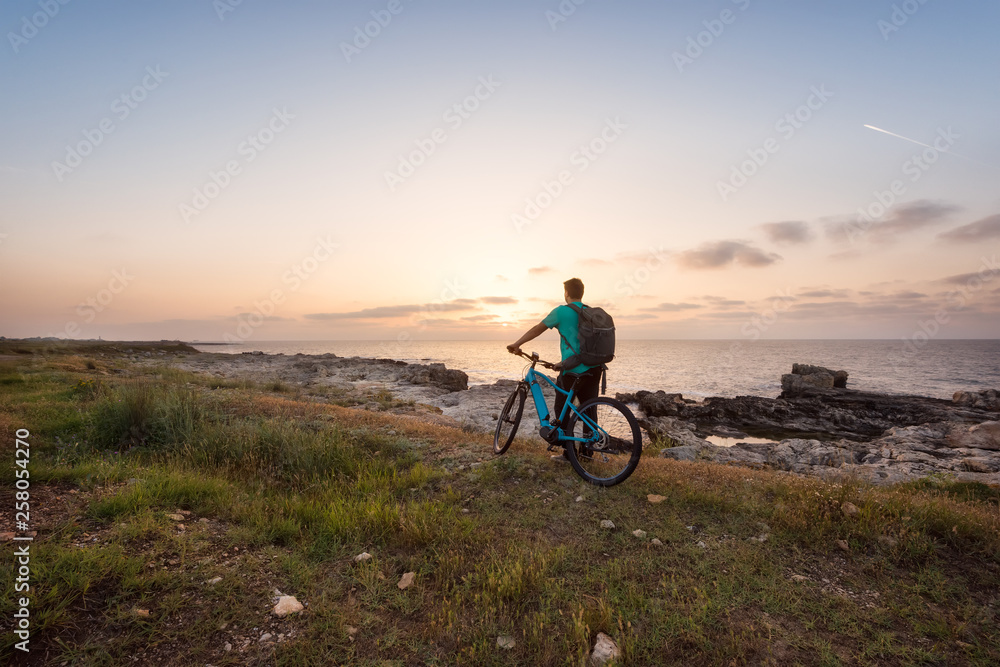 Man with a bike in the nature / Rear view of a man with a backpack and a bike enjoys the view of sunrise at the Black Sea coast