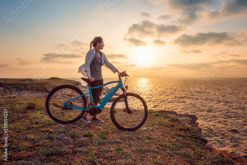 Woman with a bike in the nature / Morning view of a woman with a bike enjoys the view of sunrise at the rocky Black Sea coast