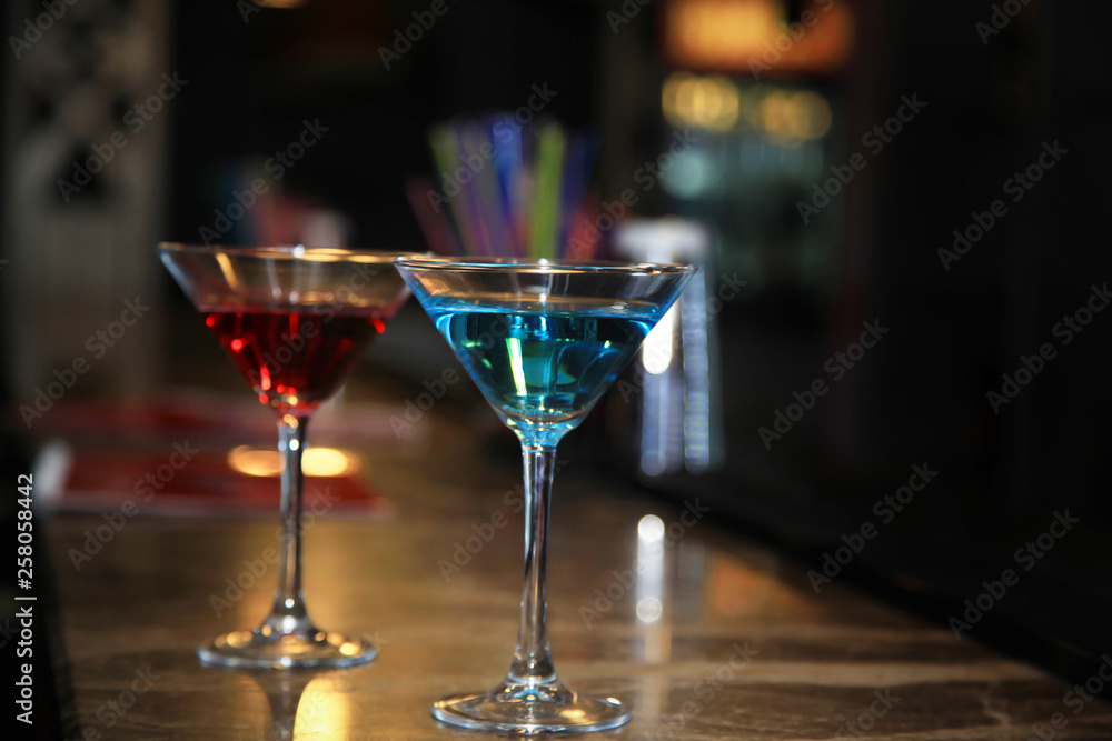 Photography of two martini glasses filled with a colored cocktails standing on the bar counter.
