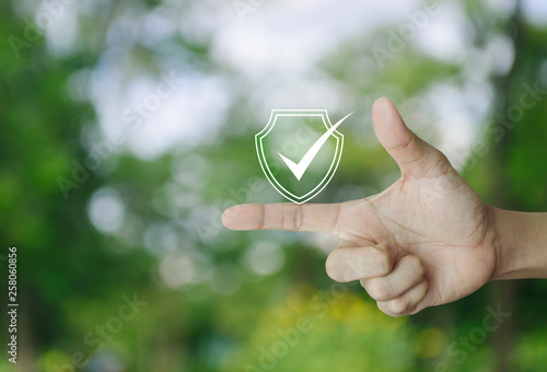 Security shield with check mark icon on finger over blur green tree in park, Technology internet cyber security and anti virus concept