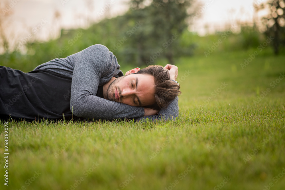 Young teenage man sleeping in the park, lying down in the grass, relaxing in nature Young teenage man sleeping in the park, lying down in the grass, relaxing in nature