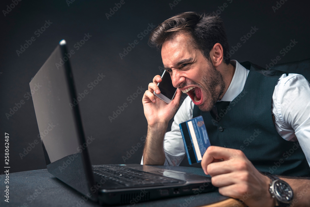 Credit card fraud, young handsome business man shouting and screaming at his bank about his credit card balance Credit card fraud, young handsome business man shouting and screaming at his bank about his credit card balance