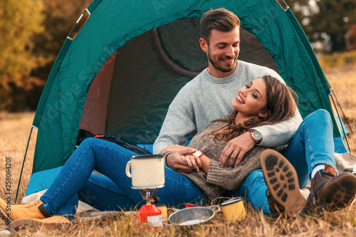 Young couple on a camping holiday, they siting in front of the tent and relaxing.