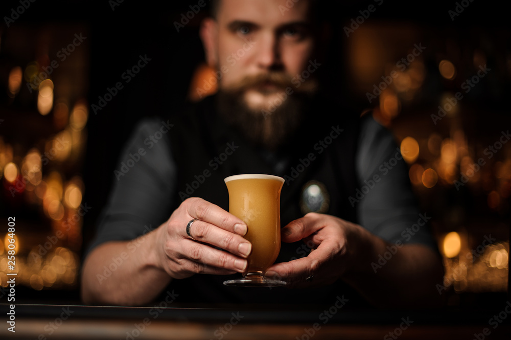 Professional bartender with a beard serving a cocktail in the glass with foam decorated with a one red rose bud
