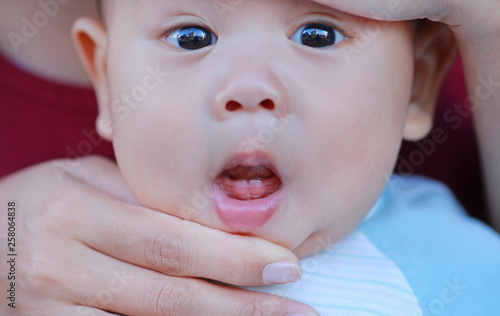 Close-up mother hands open baby mouth to examine first teeth. Infant primary tooth.