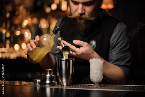 Bartender pouring a delicious alcoholic drink from the steel jigger