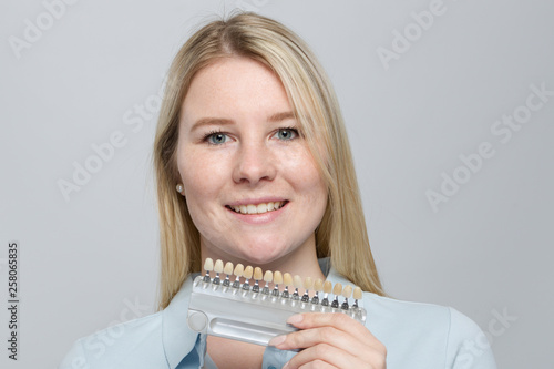 Using a shade guide at mouth of a young woman to check veneer of teeth
