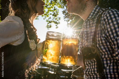 Paar im Biergarten hält Maß Bier in den Händen, Annäherung im Gegenlicht