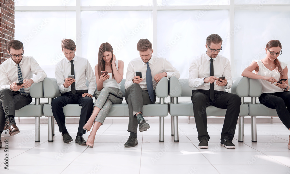 group of young employees sitting in a row in the office waiting room group of young employees sitting in a row in the office waiting room
