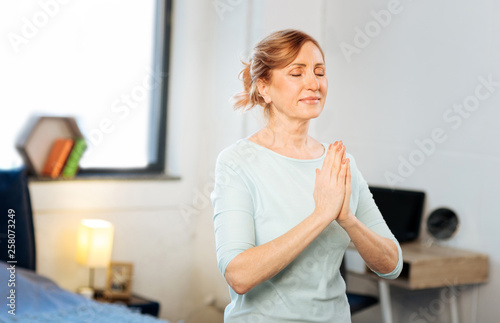 Appealing mature lady being in peaceful state while meditating
