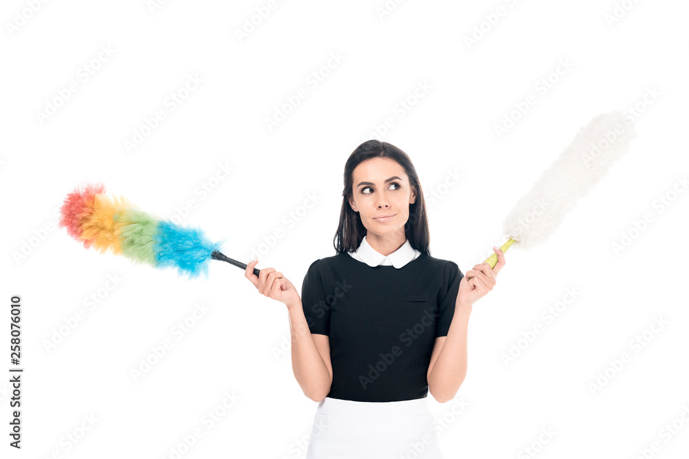 Dreamy brunette maid in uniform holding dusters isolated on white