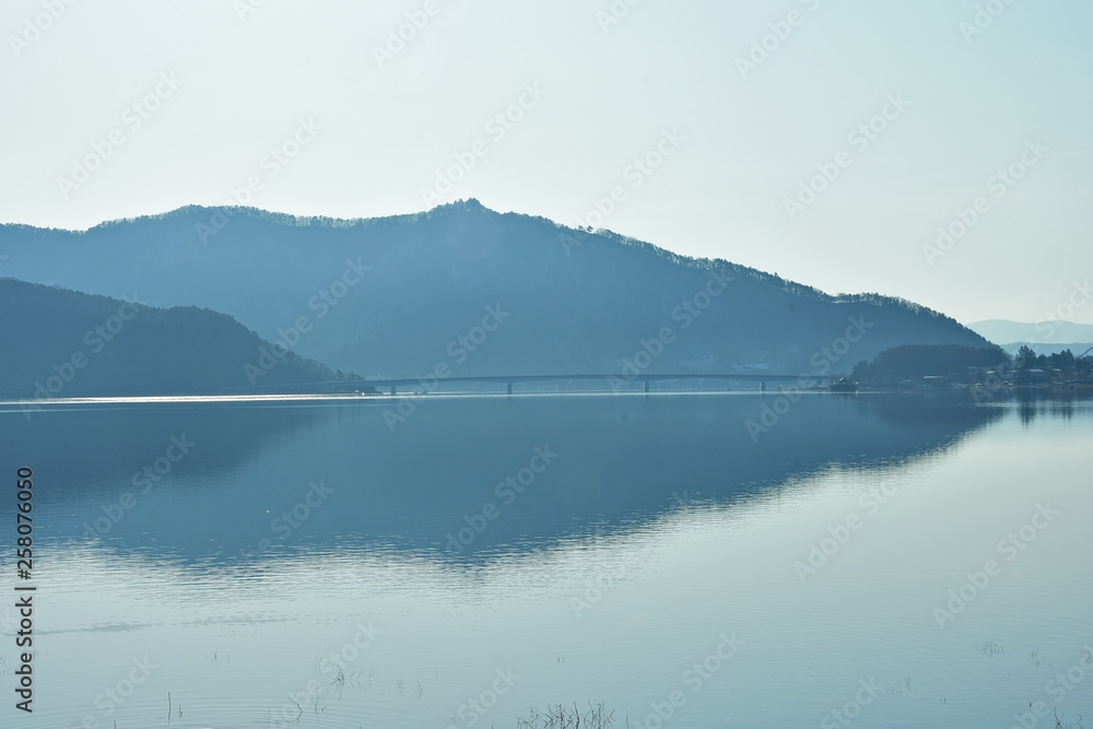 The mountain background with a bridge across the large lake has a steady water.