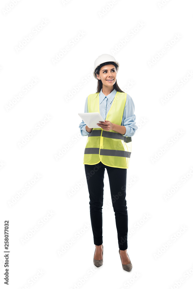 Full length view of dreamy engineer in safety vest using digital tablet isolated on white Full length view of dreamy engineer in safety vest using digital tablet isolated on white