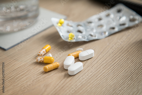 Pillen Blister mit gelben Tabletten und Wasser Glas auf Holz Nachttisch photo