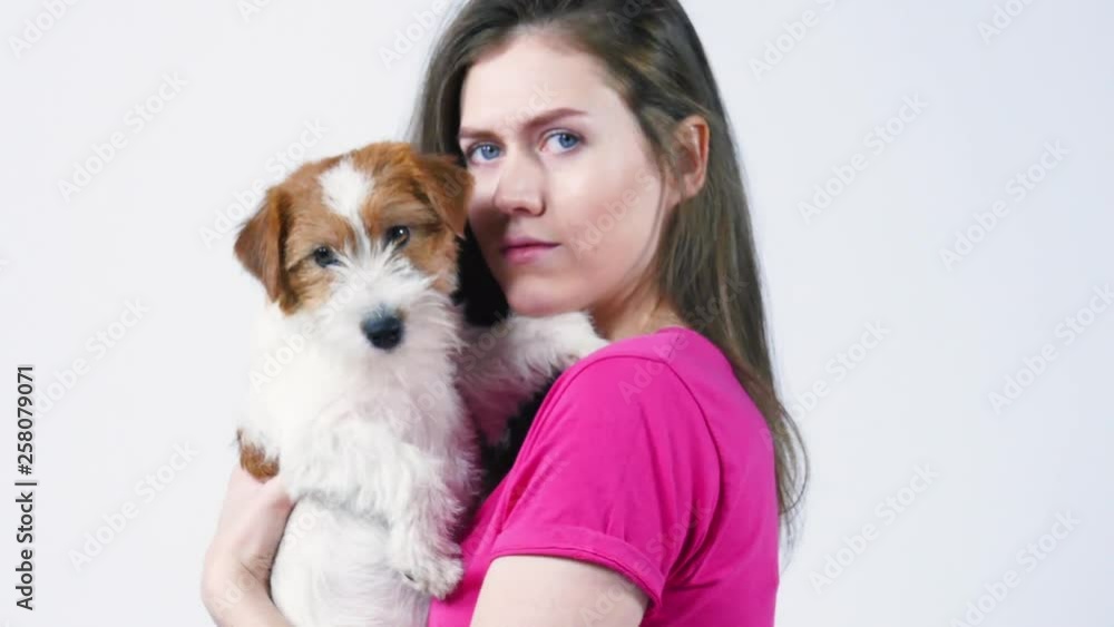 Happy beautiful girl in a pink T-shirt hugs a puppy Jack Russell Terrier, looks into the camera, gray background, close-up Happy beautiful girl in a pink T-shirt hugs a puppy Jack Russell Terrier, looks into the camera, gray background, close-up