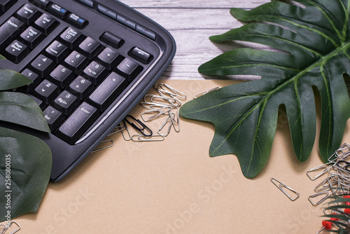 Flat lay, top view office table desk. Workspace with blank clip board, keyboard, office supplies, pencil, green leaf on wooden background. office products and stationery framed. Notebook