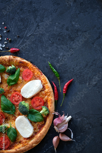 Italian pizza with Mozzarella cheese, tomatoes, broccoli, Spices and fresh basil. Pizza on black stone background