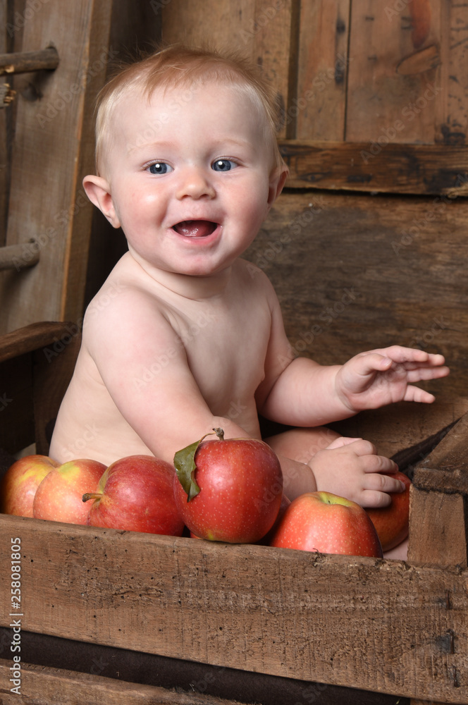 child in a crate with apples