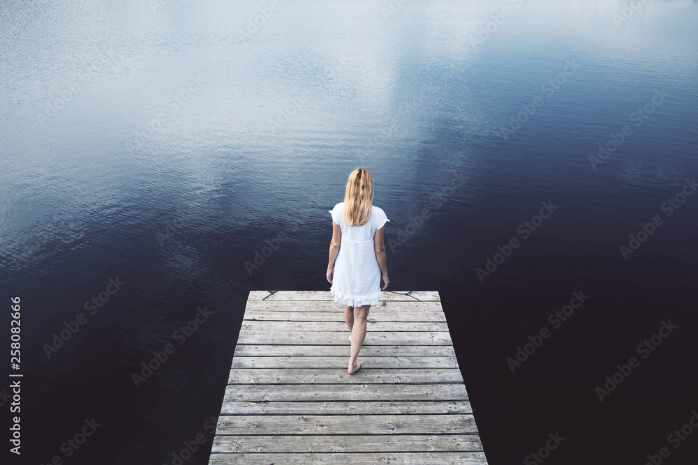 Woman alone walks on wooden pier at dark blue lake. Woman alone walks on wooden pier at dark blue lake.