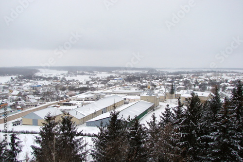 Panorama of the town of Pochayiv in the Ternopil region on a snowy winter day surrounded by a high pine forest against a background of cloudy gray sky. photo