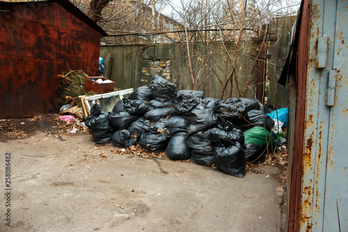 black bags of construction garbage lie between two garages in the yard. garbage bag black bin waste background.