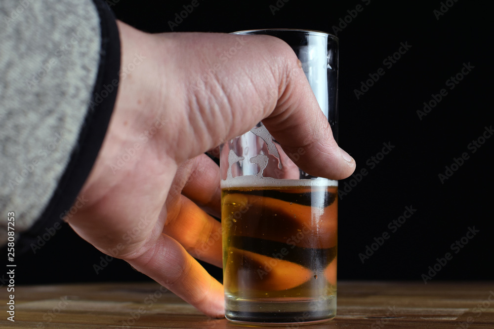 Male hand taking a glass of beer from wood table. Black background with copy space. Male hand taking a glass of beer from wood table. Black background with copy space.