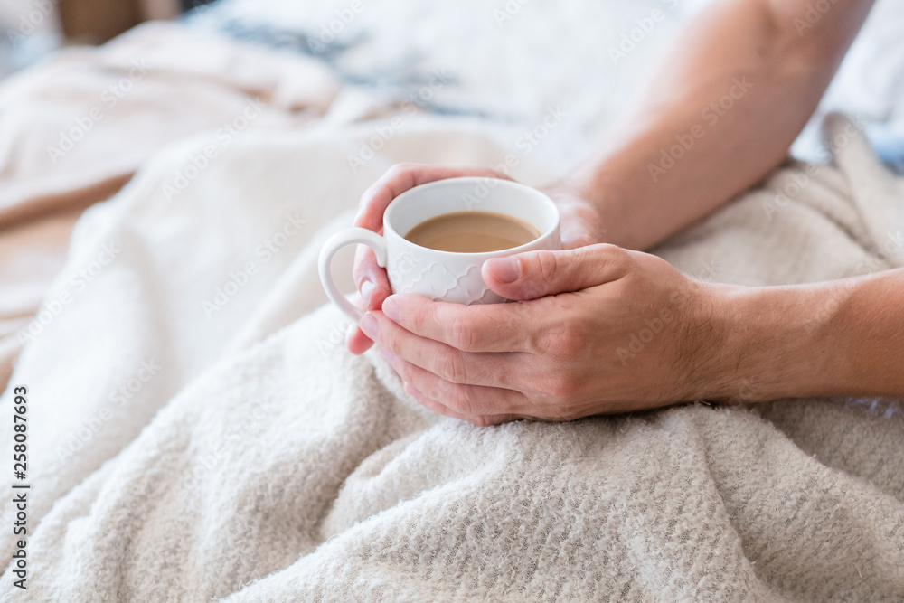 Morning coffee warmth and energy. New day habit. Man in bed. Hands around white cup of latte. Morning coffee warmth and energy. New day habit. Man in bed. Hands around white cup of latte.