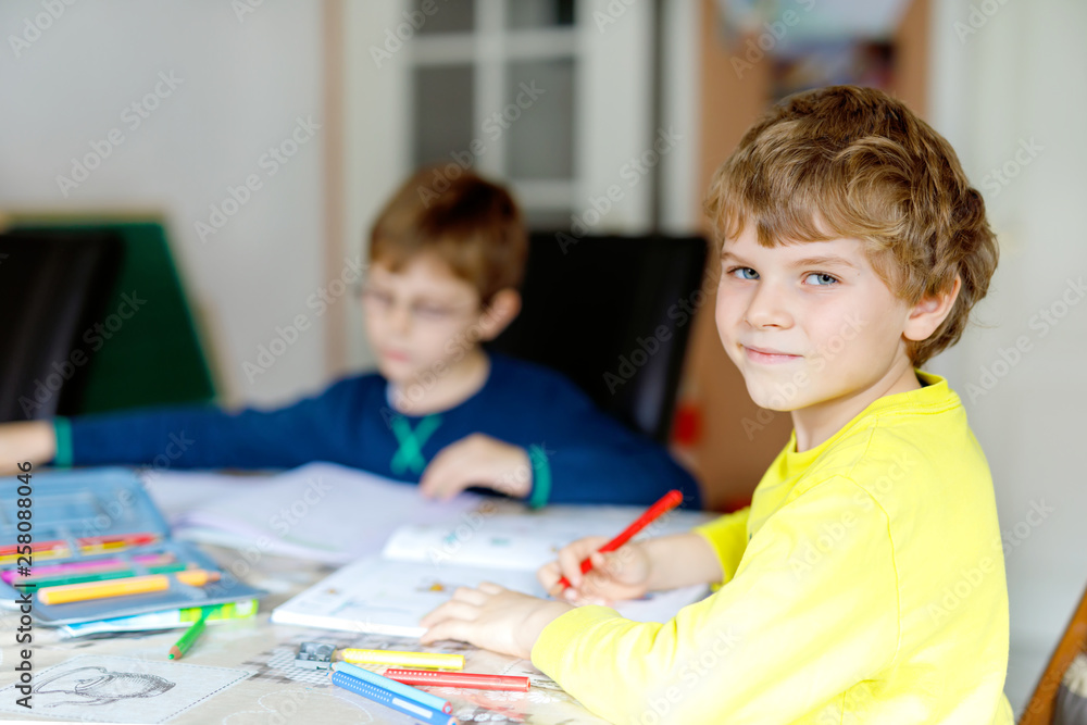 Two little kids boys at home making homework. Little concentrated children writing with colorful pencils, indoors. Elementary school and education. Siblings and best friends learning. Two little kids boys at home making homework. Little concentrated children writing with colorful pencils, indoors. Elementary school and education. Siblings and best friends learning.