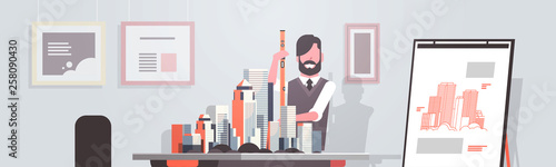 man architect holding level engineer working with new building city model for urban panning project concept house blueprint modern office studio interior horizontal portrait