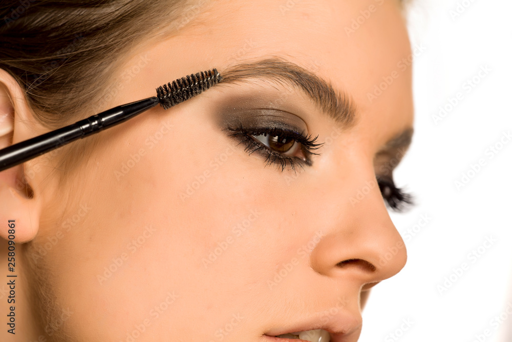 Young woman shaping her eyebrows with brush on white background