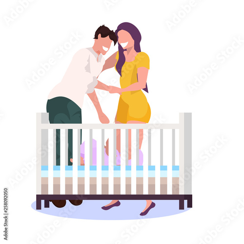 happy couple parents standing near baby crib husband with wife embracing and looking at newborn baby lying in cot parenthood concept flat full length