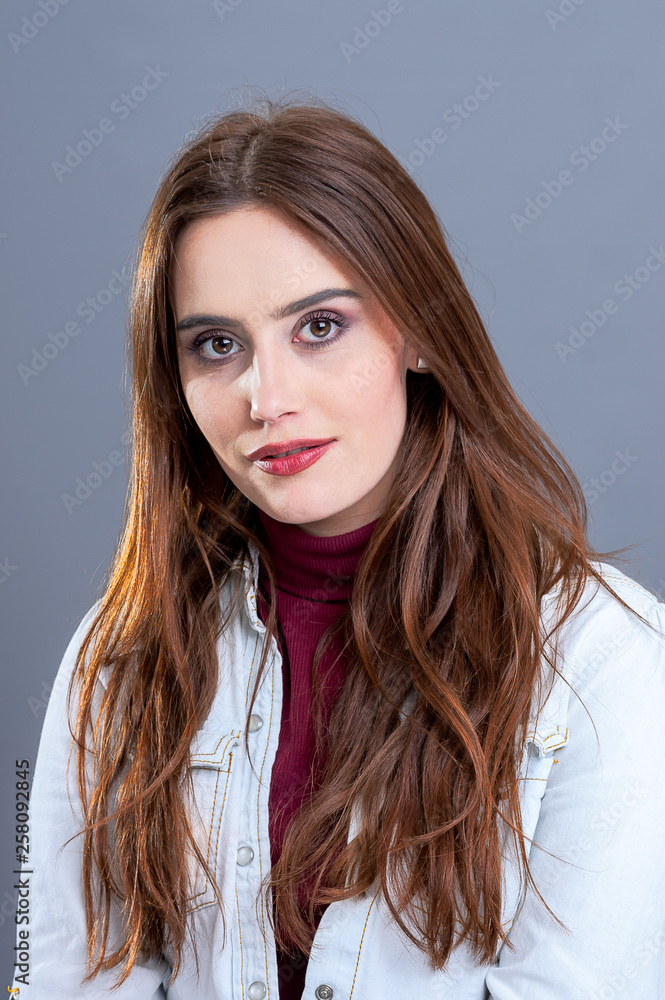 Portrait of Emily wearing a blue shirt over a red roll neck, shot against a grey background