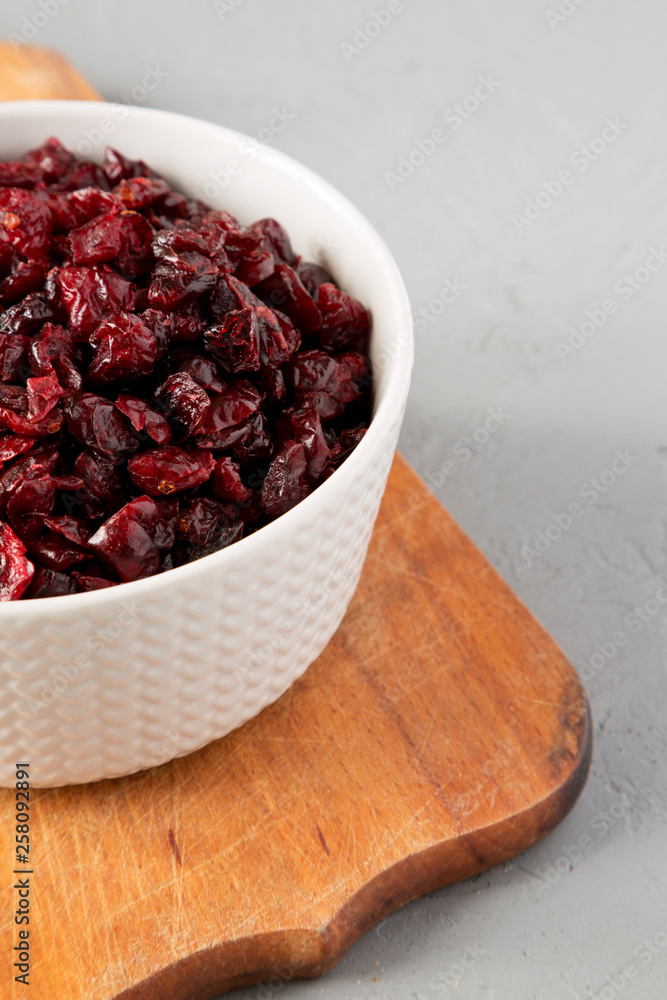 Dried cranberries in a bowl on rustic wooden board over concrete background, side view. Close-up. Dried cranberries in a bowl on rustic wooden board over concrete background, side view. Close-up.