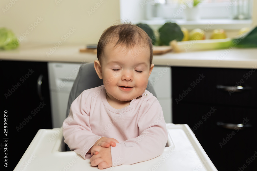 The baby is sitting at the children's chair and waiting for her mother to feed her. The baby is sitting at the children's chair and waiting for her mother to feed her.