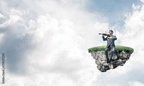 Handsome violinist on floating island in blue sky play his melody